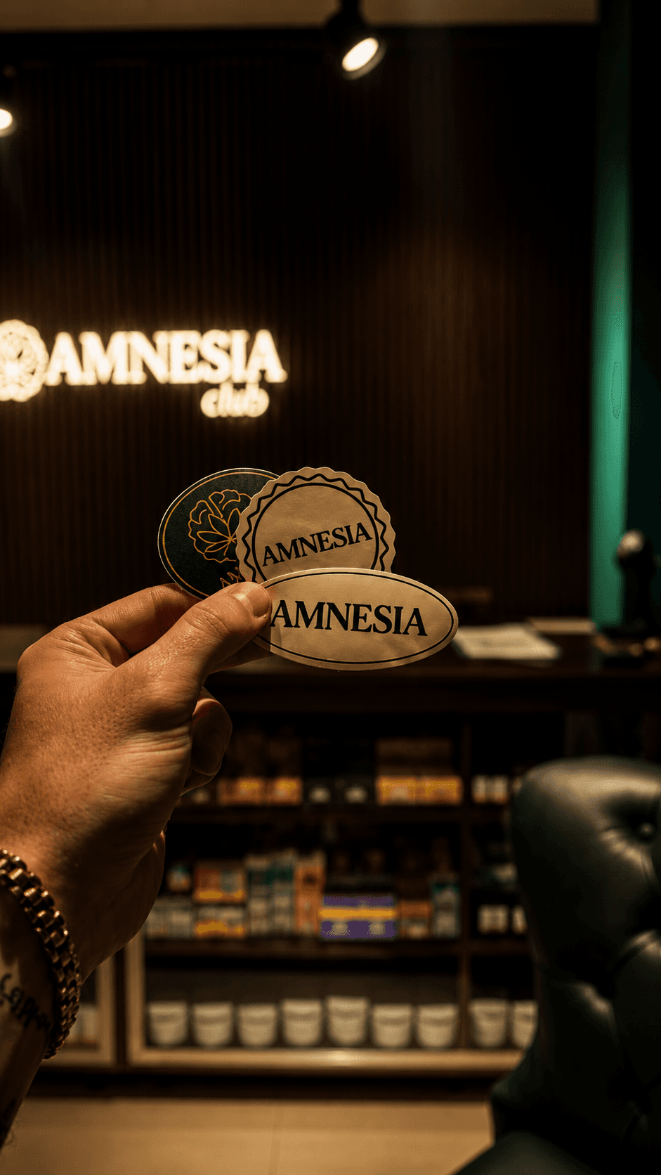Stickers Amnesia Clvb en mano con fondo del salón